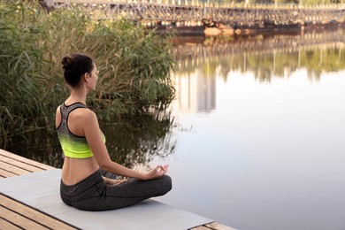 Photo of Woman meditating on wooden pier near river. Space for text
