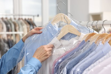 Photo of Dry-cleaning service. Woman taking shirt in plastic bag from rack indoors, closeup
