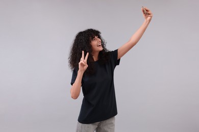 Photo of Beautiful young woman taking selfie on light grey background