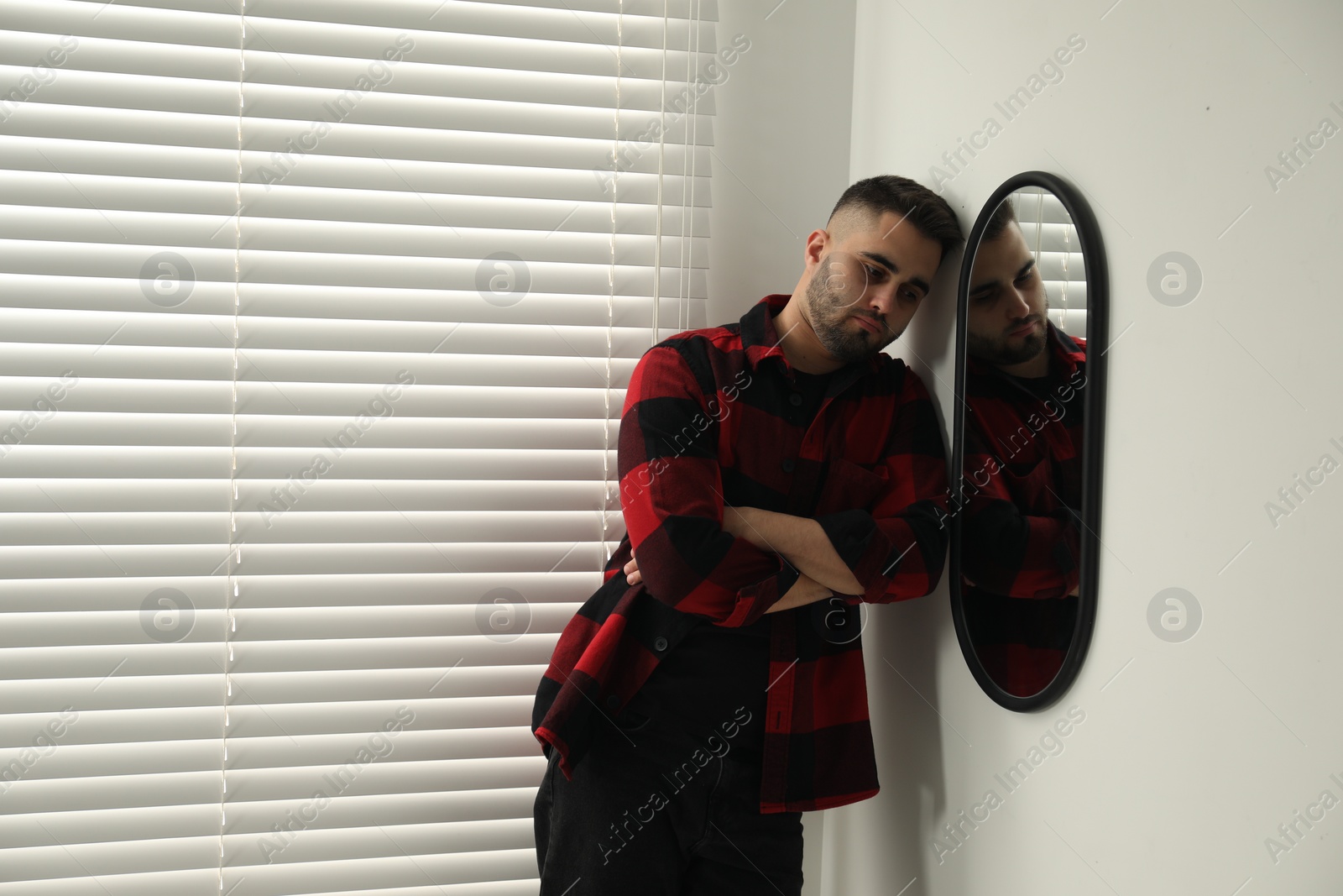 Photo of Sad young man near mirror at home. Space for text
