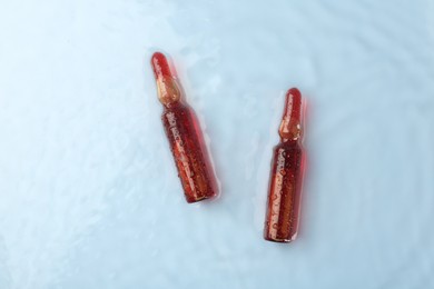 Photo of Skincare ampoules in water on light blue background, top view