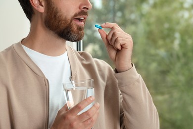 Man with glass of water taking pill indoors, closeup. Space for text