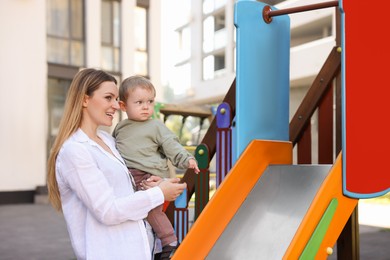 Photo of Happy nanny with cute little boy near slide outdoors