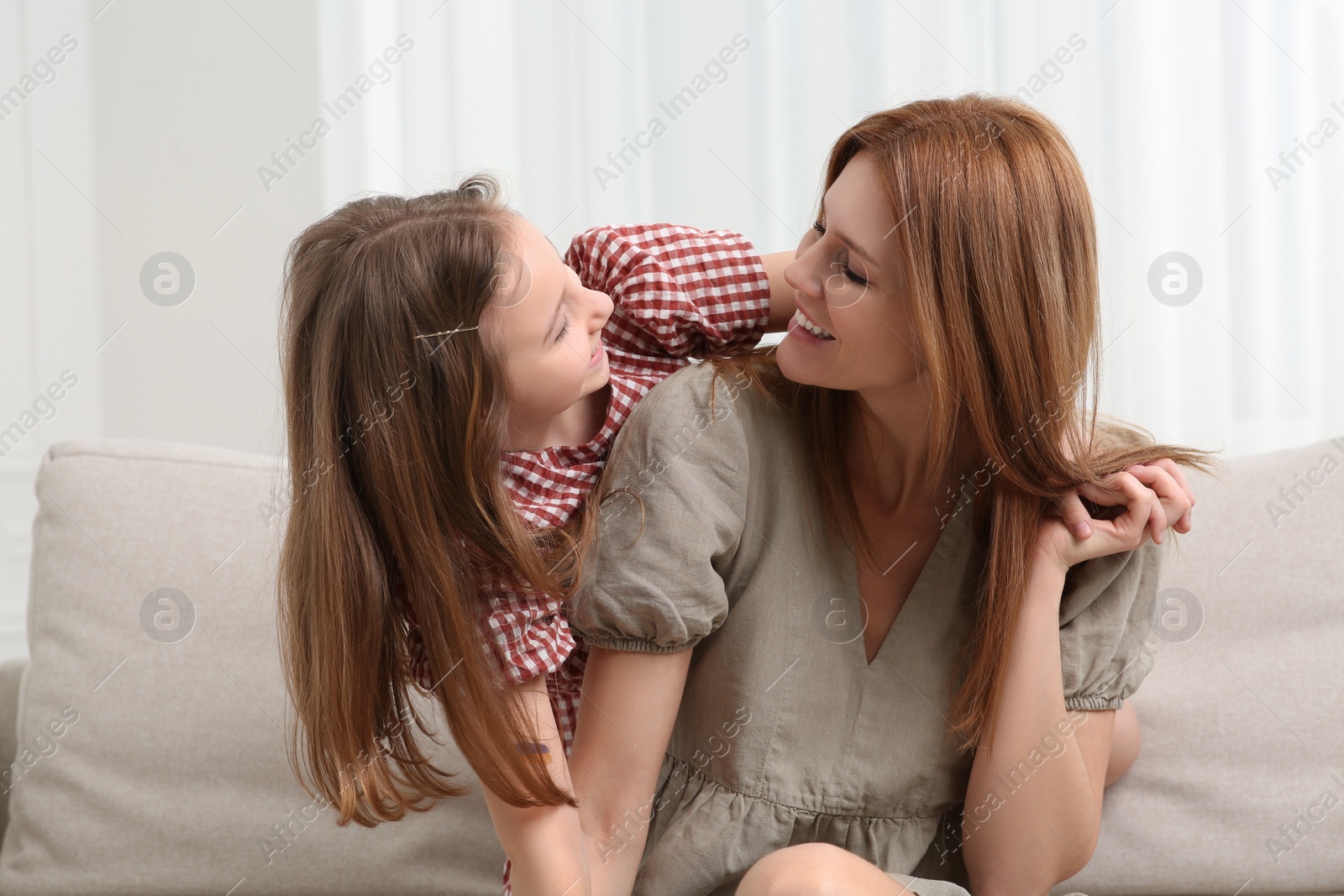 Photo of Mother with her cute daughter spending time together on sofa at home