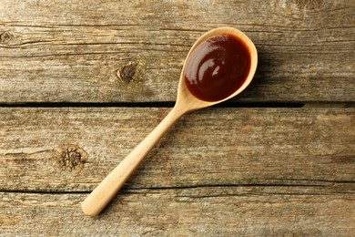 Photo of Spoon with tasty barbeque sauce on wooden table, top view