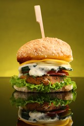 Photo of Delicious vegetarian burger on mirror surface against olive background