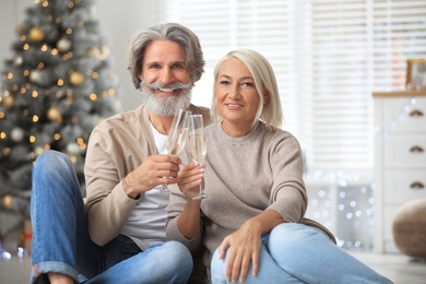 Happy mature couple with glasses of champagne celebrating Christmas at home