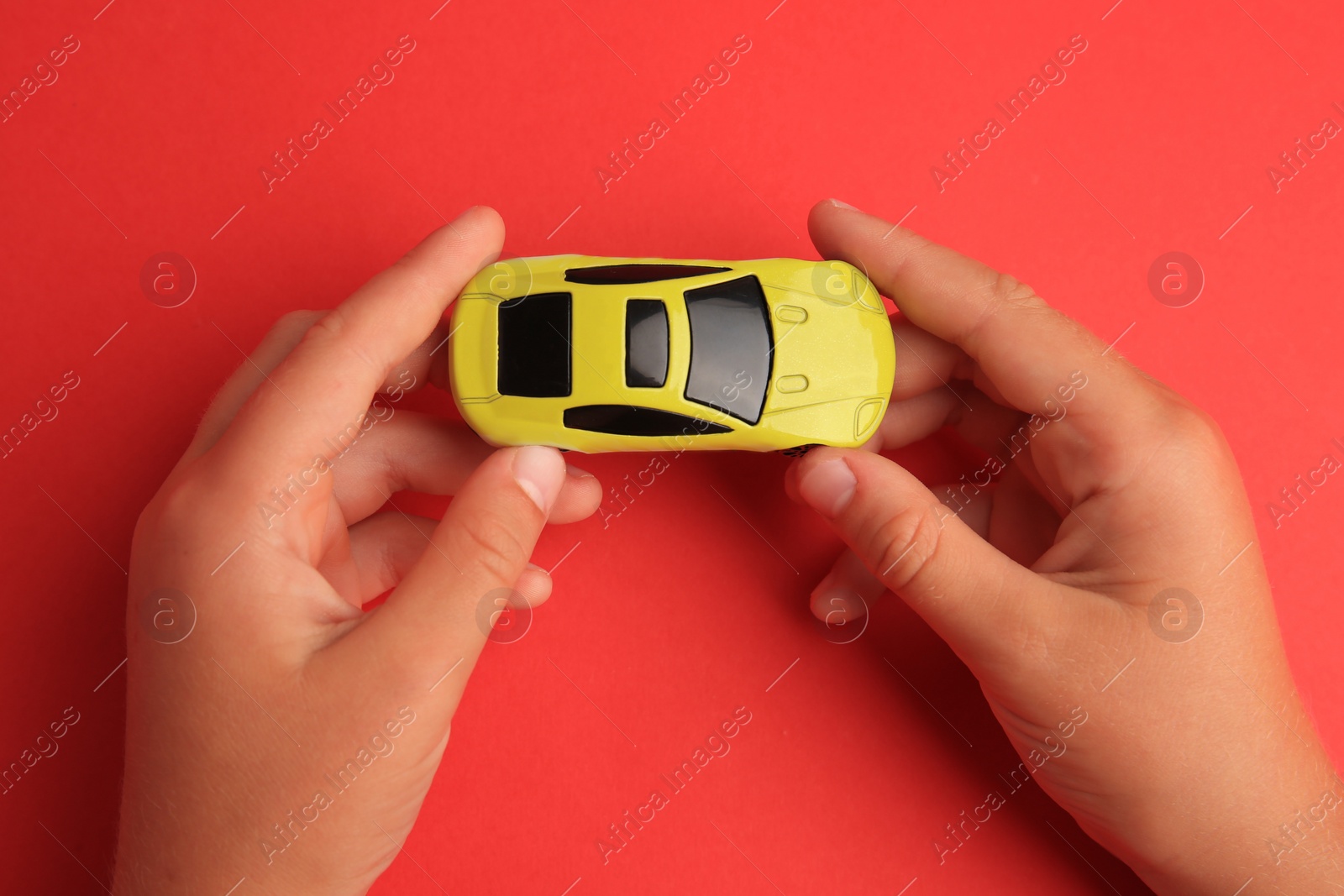 Photo of Child holding toy car on red background, top view