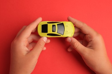 Child holding toy car on red background, top view