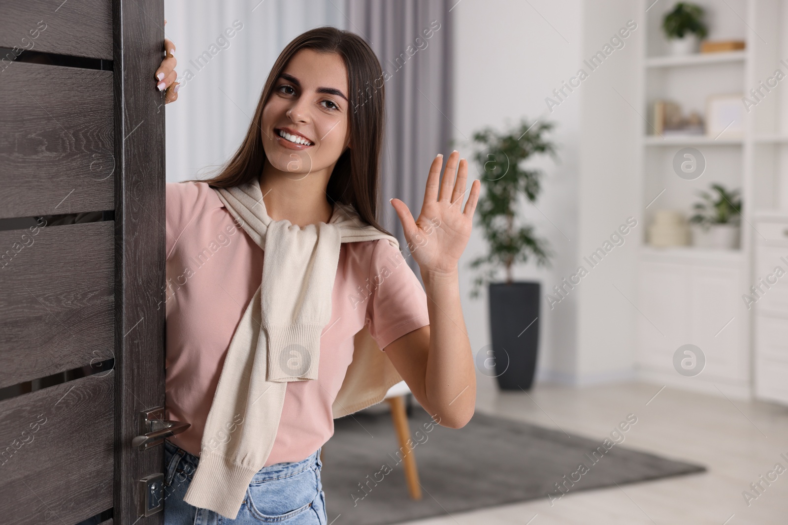 Photo of Happy woman waving near door, space for text. Invitation to come indoors