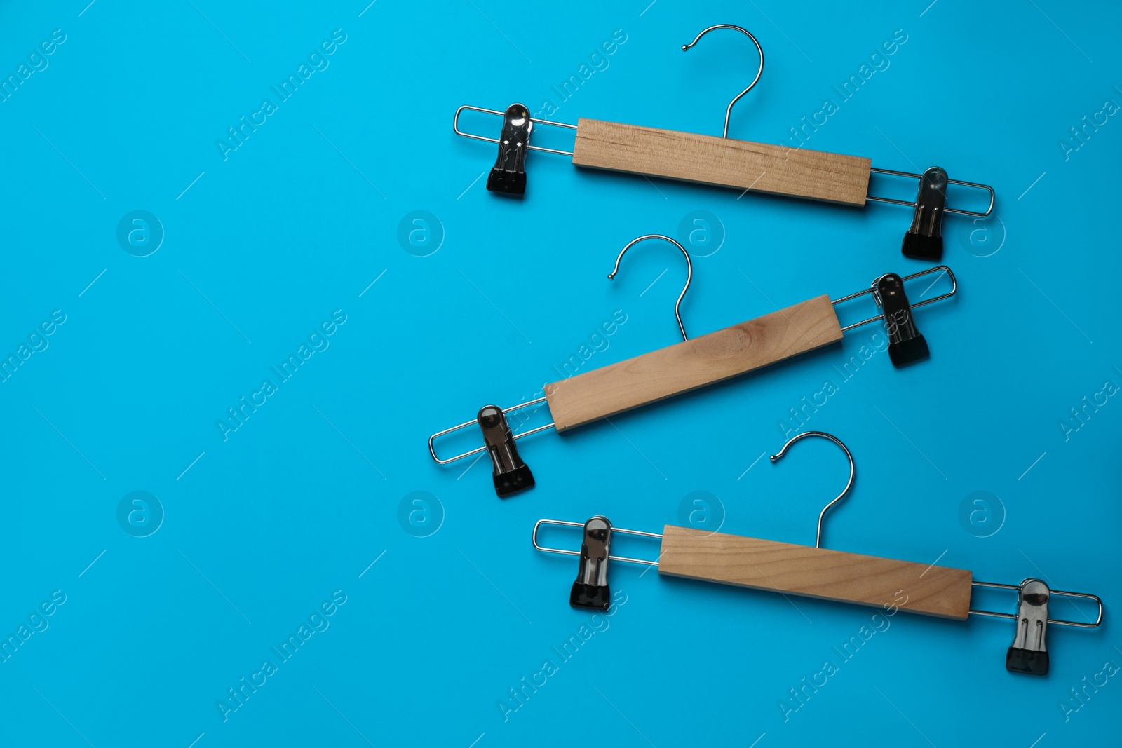 Photo of Empty wooden hangers with clips on light blue background, flat lay. Space for text