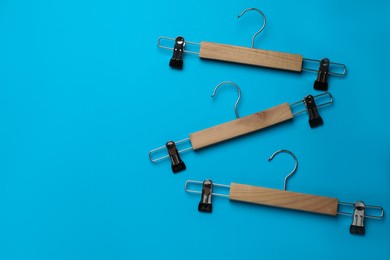 Photo of Empty wooden hangers with clips on light blue background, flat lay. Space for text