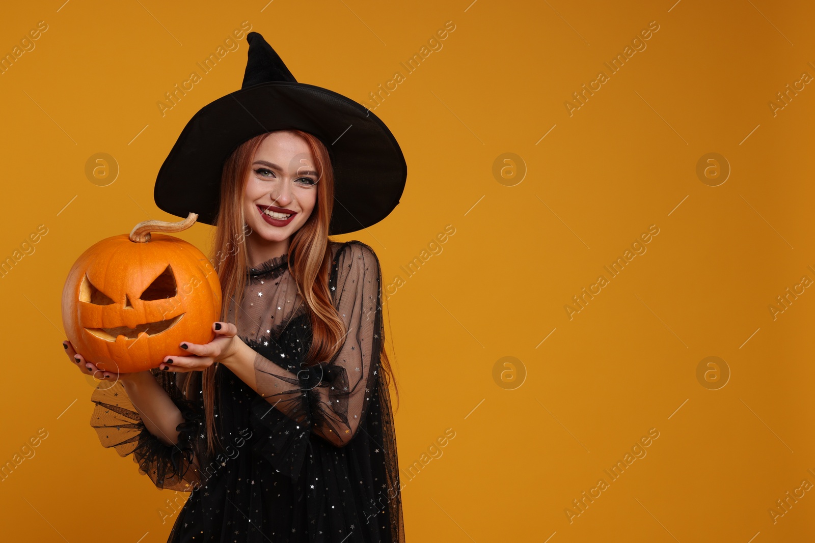 Photo of Happy young woman in scary witch costume with carved pumpkin on orange background, space for text. Halloween celebration