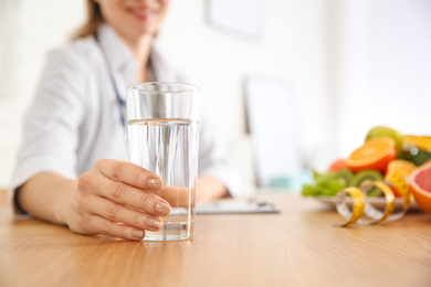 Nutritionist with glass of water at desk in office, closeup