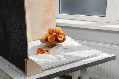 Photo of Stand with juicy peaches and double-sided backdrops on table in photo studio