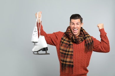 Emotional man with ice skates on grey background