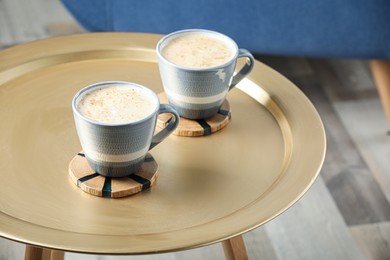 Photo of Mugs of coffee with stylish cup coasters on table in room