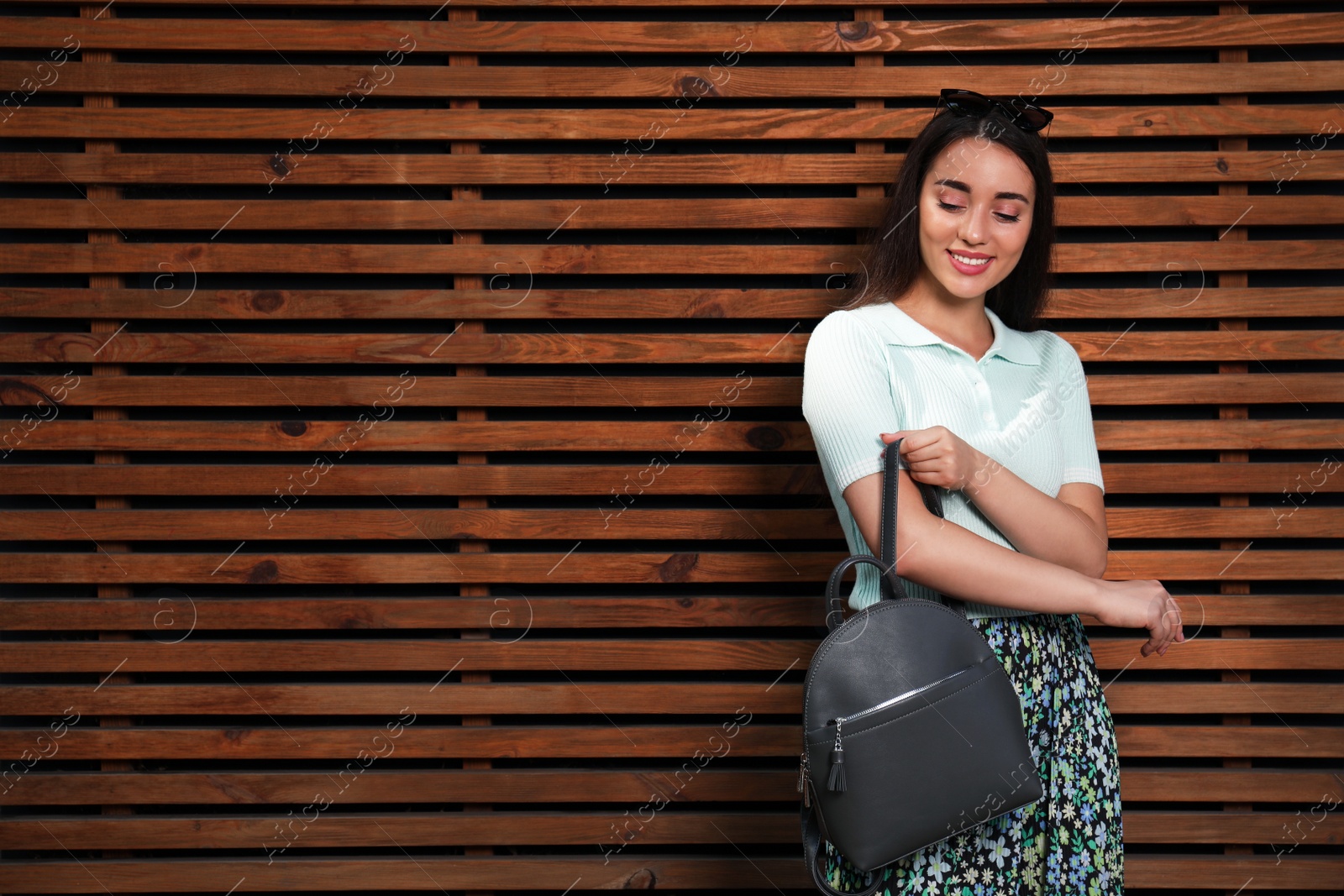Photo of Beautiful young woman with stylish backpack near wood slat wall, space for text