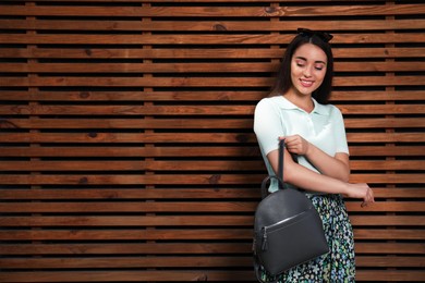 Beautiful young woman with stylish backpack near wood slat wall, space for text