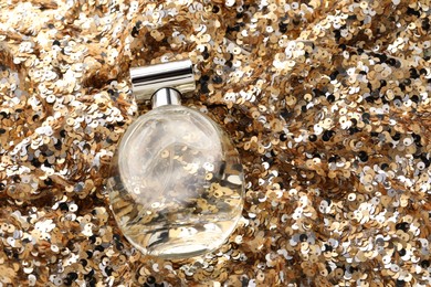 Photo of Luxury perfume in bottle on fabric with golden sequins, above view