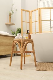 Photo of Different spa products on wicker table near ceramic tub in bathroom