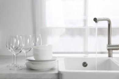 Photo of Different clean dishware and glasses on countertop near sink in kitchen