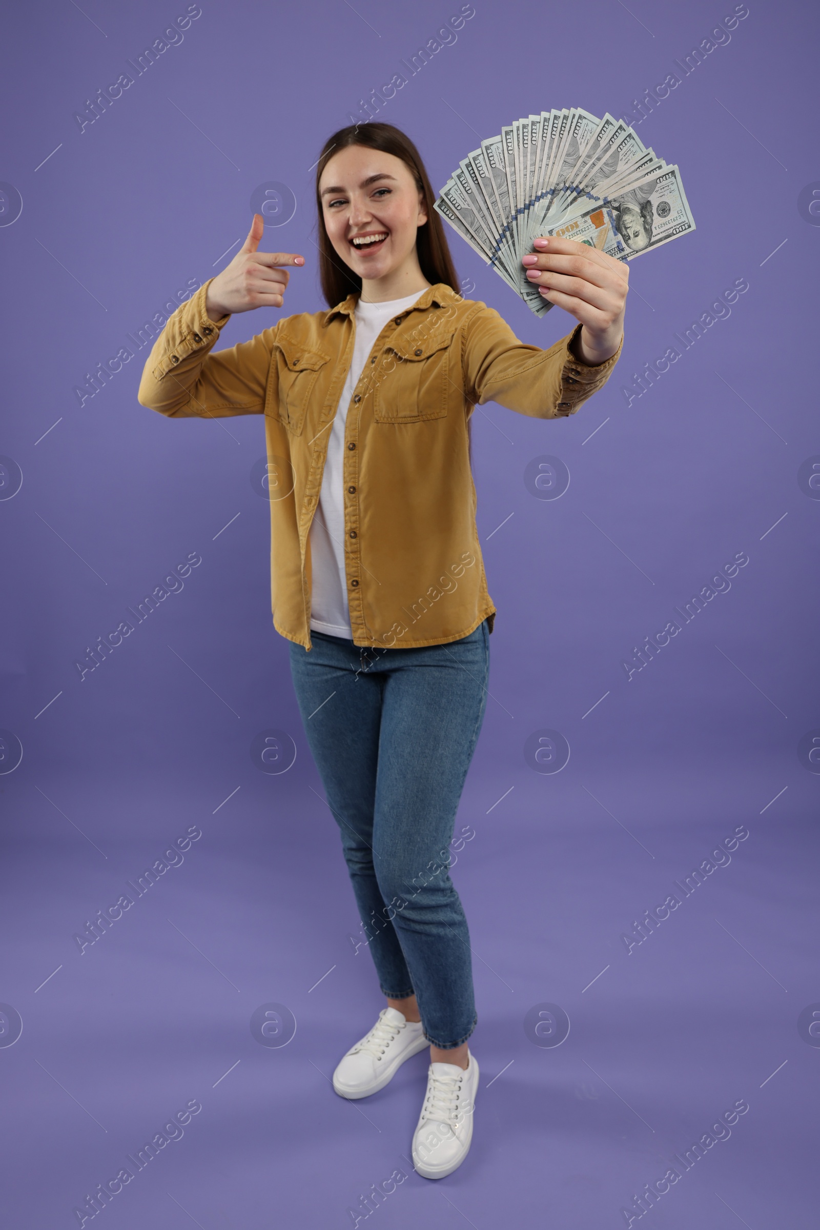 Photo of Happy woman pointing at dollar banknotes on purple background