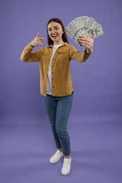 Happy woman pointing at dollar banknotes on purple background