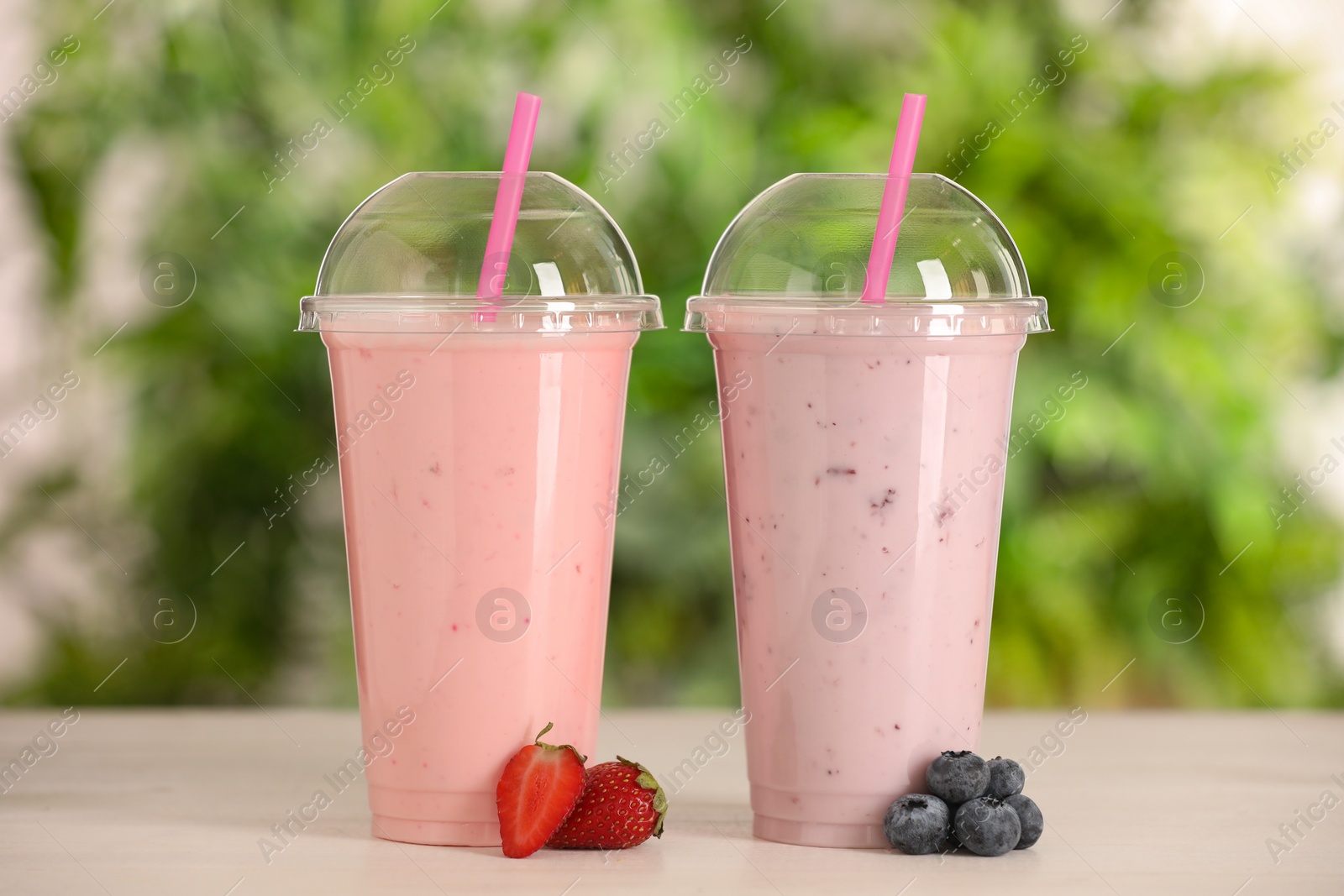 Photo of Plastic cups with different tasty smoothies and fresh fruits on wooden table outdoors