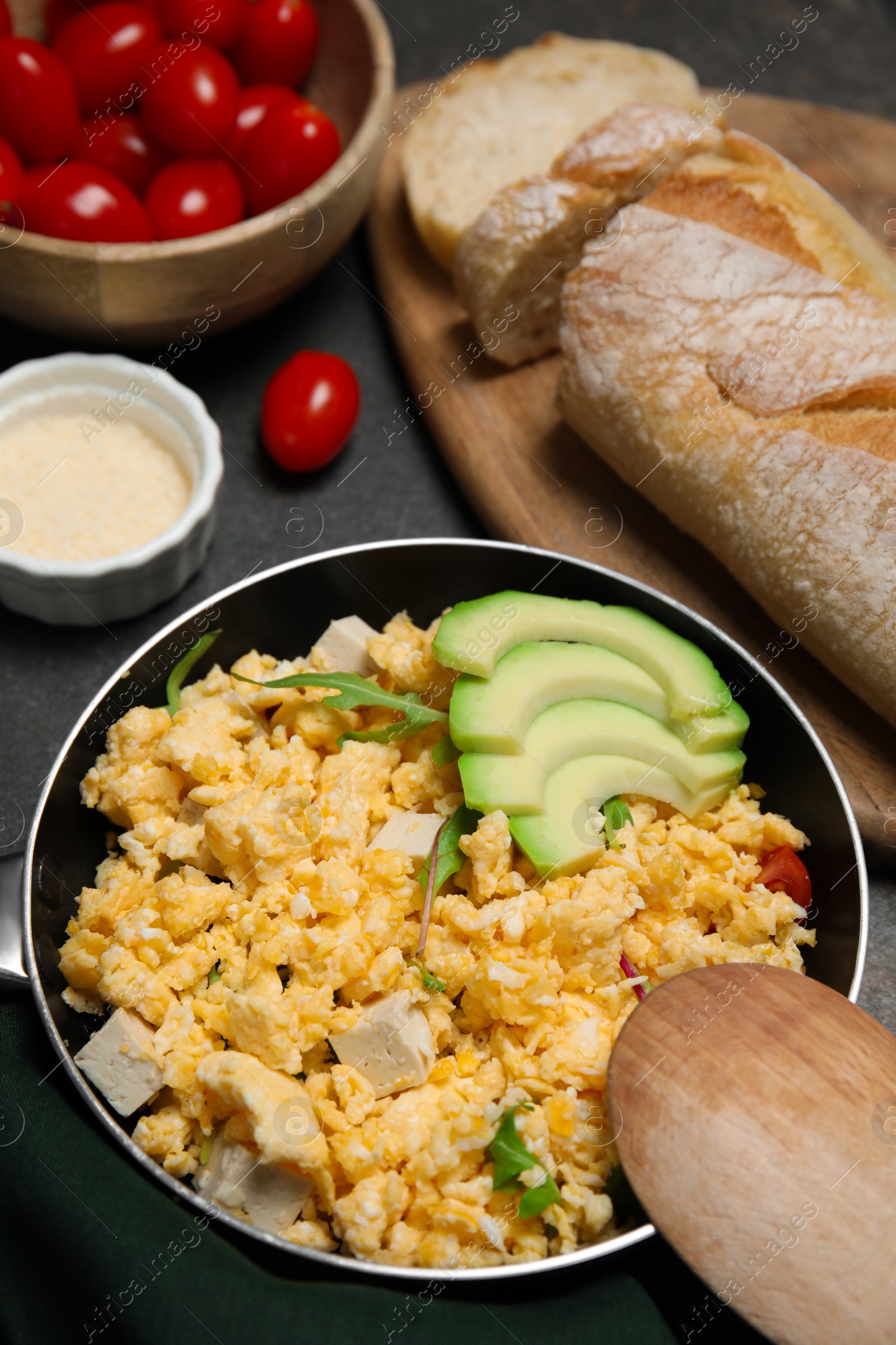 Photo of Frying pan with delicious scrambled eggs, tofu and avocado on black table