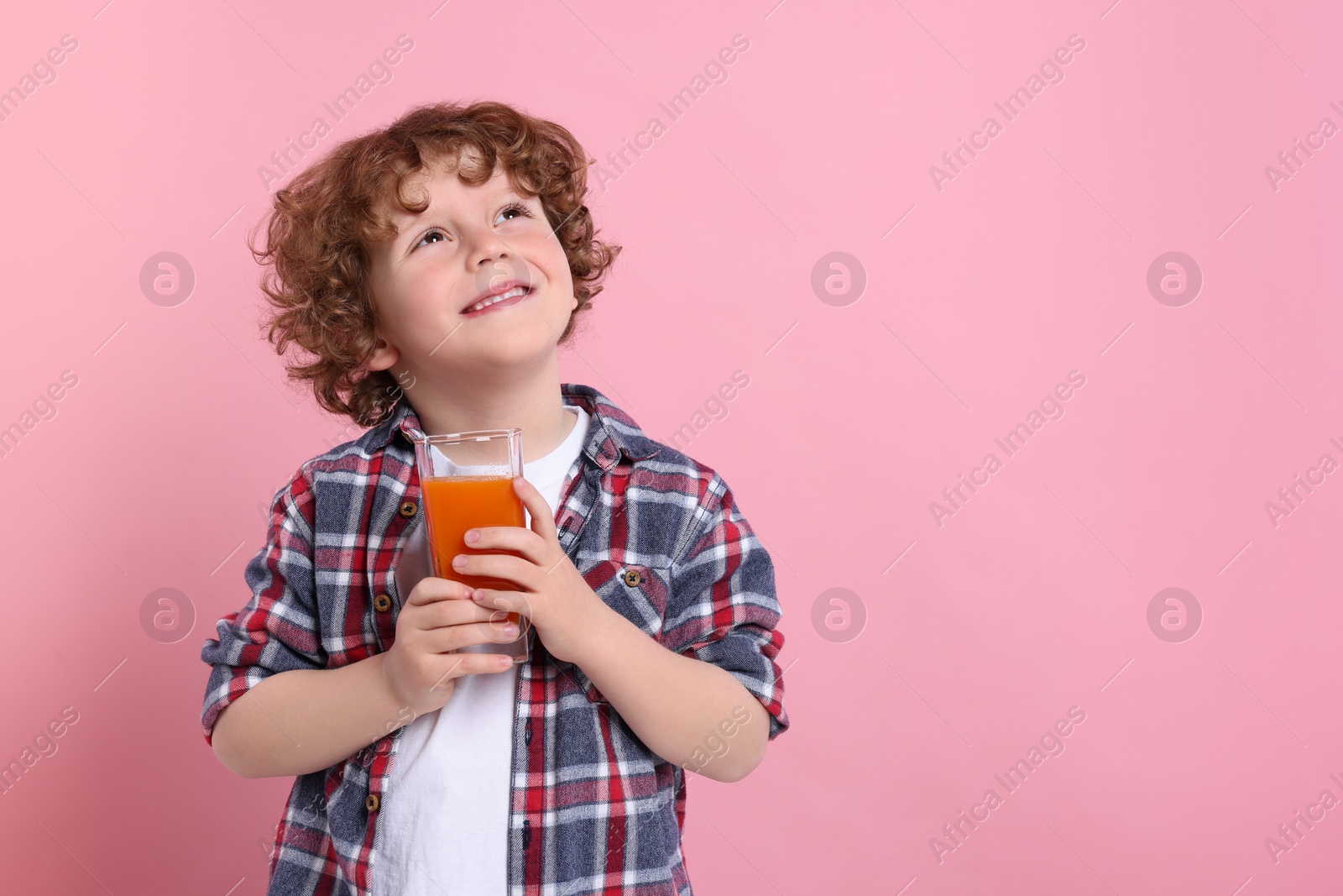 Photo of Cute little boy with glass of fresh juice on pink background, space for text