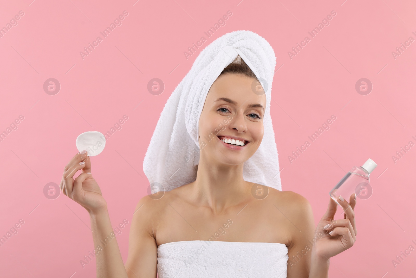 Photo of Removing makeup. Smiling woman with cotton pad and bottle on pink background