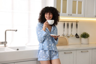 Photo of Beautiful young woman in stylish pyjama with cup of drink in kitchen