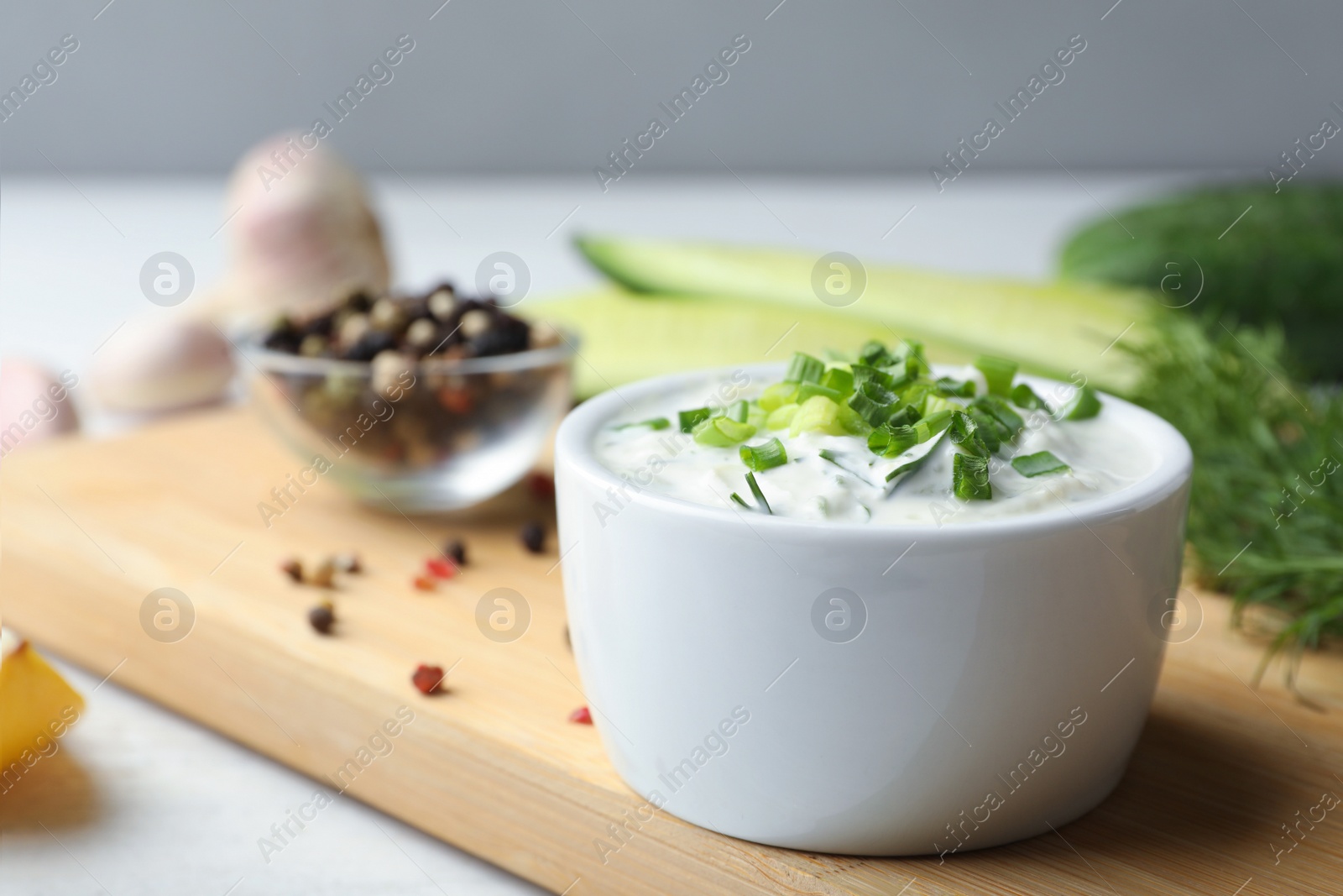 Photo of Ceramic bowl of cucumber sauce with ingredients on wooden table, space for text. Traditional Tzatziki