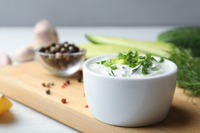 Photo of Ceramic bowl of cucumber sauce with ingredients on wooden table, space for text. Traditional Tzatziki