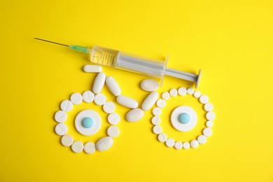 Bike made of pills and syringe on yellow background, flat lay. Using doping in cycling sport concept