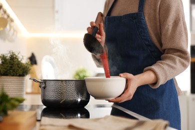 Photo of Woman pouring tasty soup into bowl at countertop in kitchen, closeup