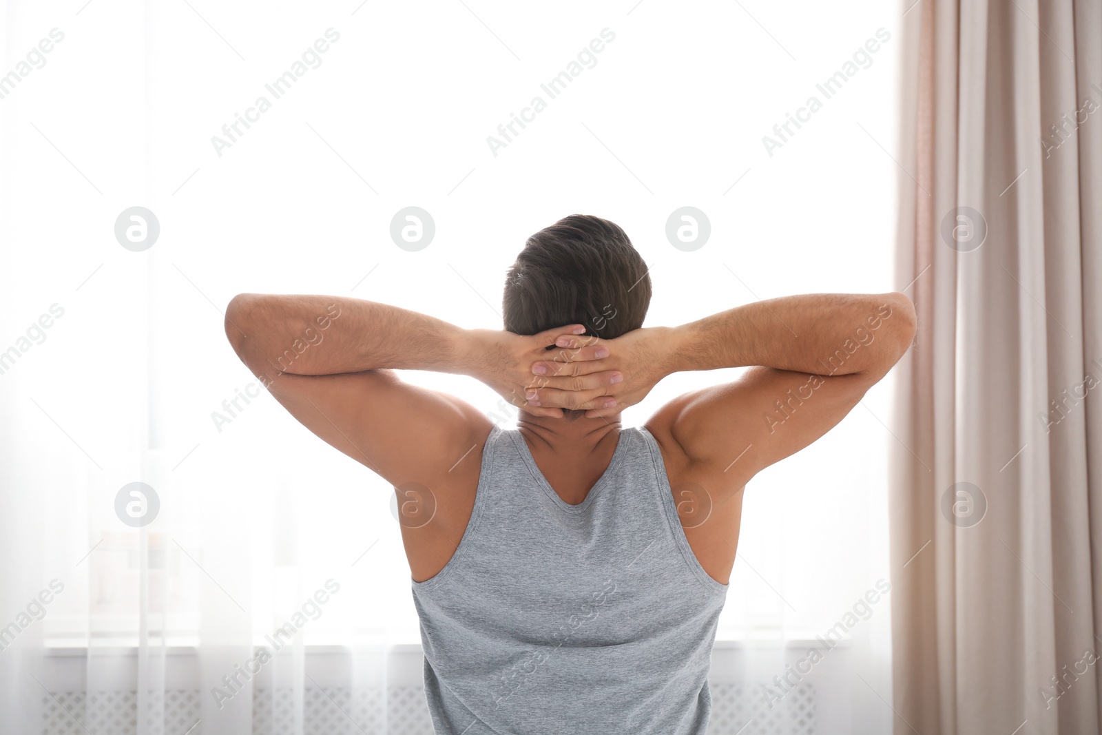 Photo of Man stretching near window at home. Lazy morning