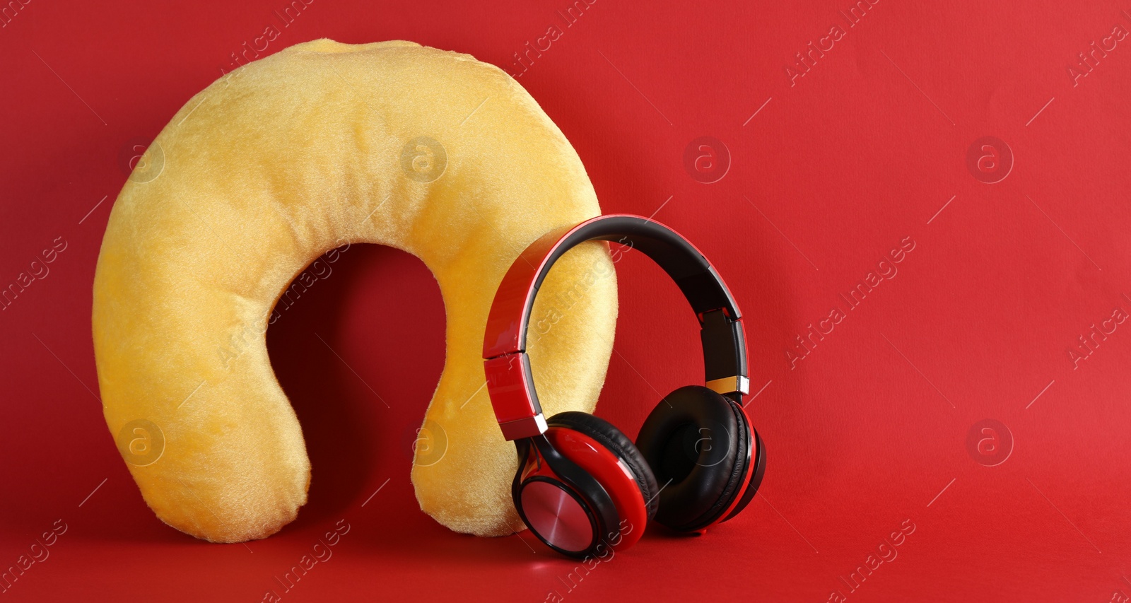 Photo of Yellow travel pillow and headphones on red background, space for text