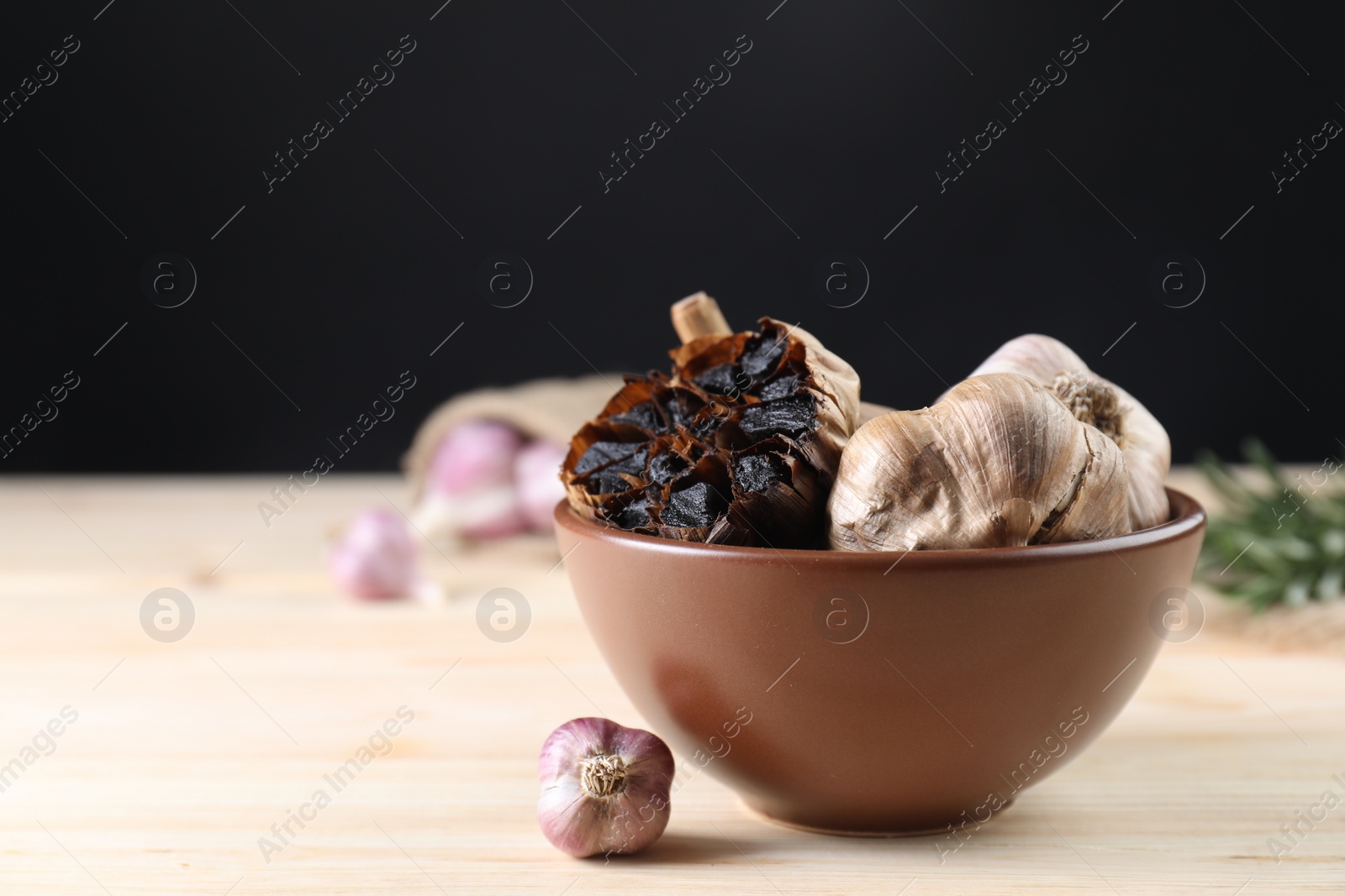 Photo of Bulbs of fresh and fermented black garlic on wooden table. Space for text