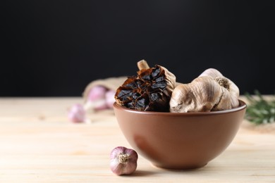 Photo of Bulbs of fresh and fermented black garlic on wooden table. Space for text