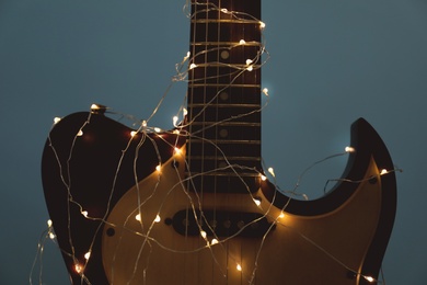 Photo of Guitar with glowing fairy lights on dark background, closeup. Christmas music