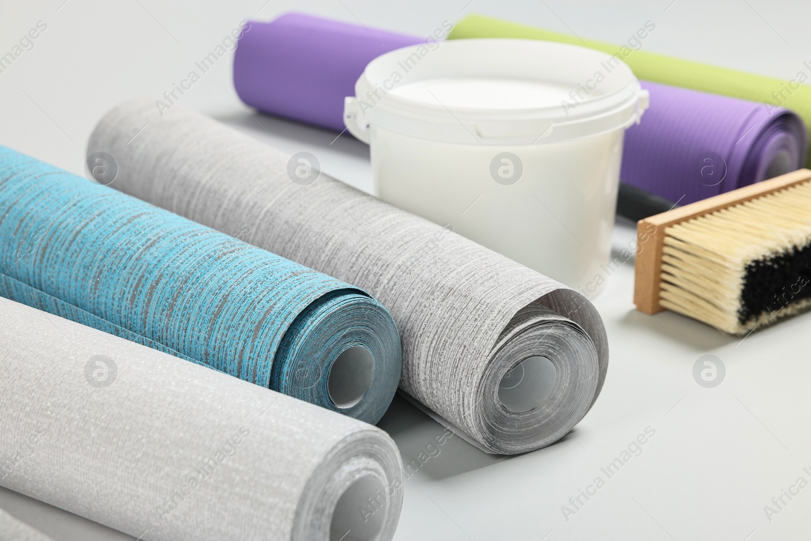 Photo of Different wallpaper rolls, brush and bucket with glue on light background