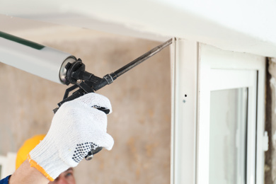 Worker using foam gun for window installation indoors, closeup