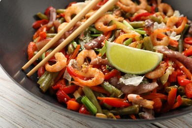 Shrimp stir fry with vegetables in wok and chopsticks on light wooden table, closeup