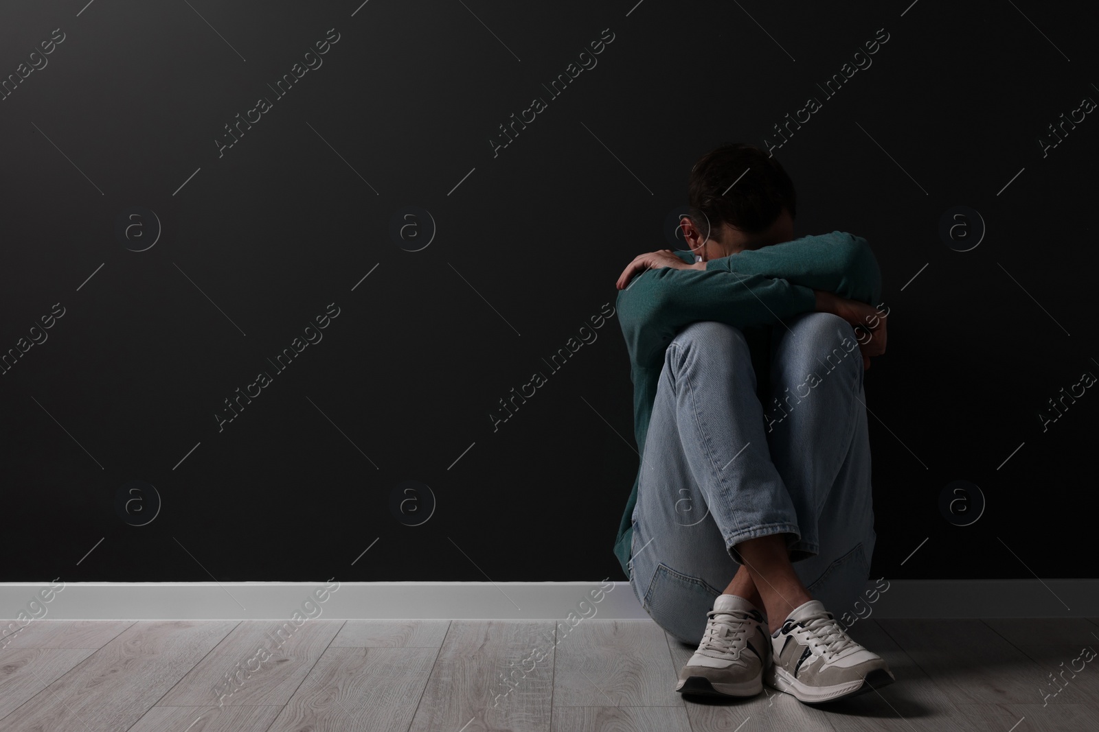Photo of Upset man sitting on floor near black wall. Space for text