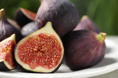 Photo of Whole and cut ripe figs on table against blurred green background, closeup