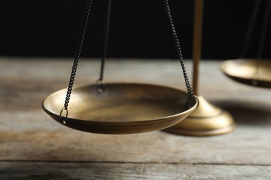 Photo of Scales of justice on wooden table against dark background, closeup. Law concept