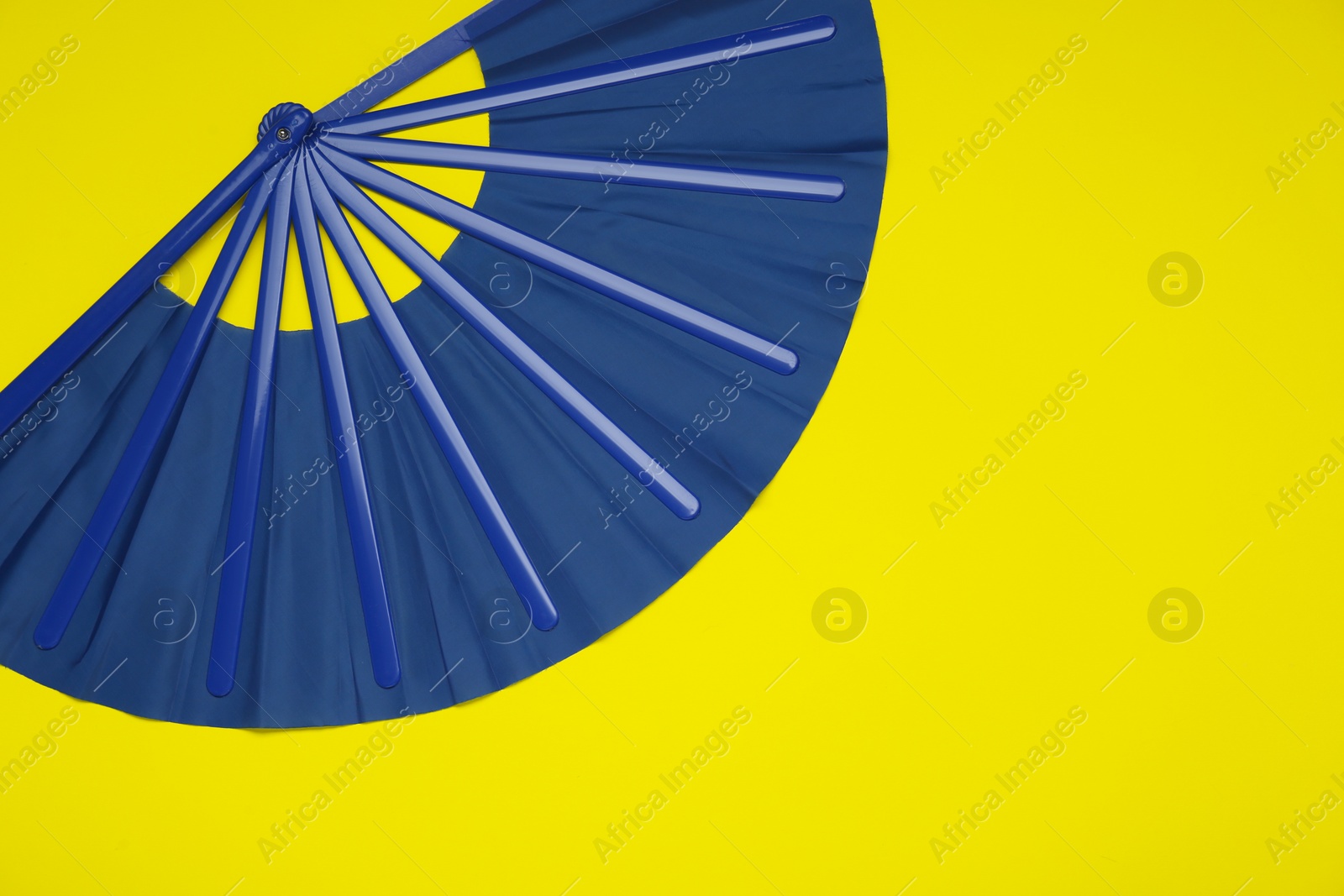 Photo of Bright blue hand fan on yellow background, top view. Space for text