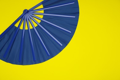 Photo of Bright blue hand fan on yellow background, top view. Space for text